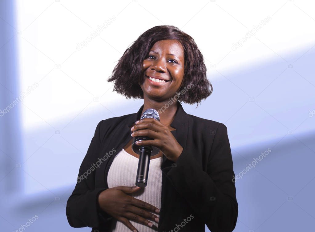  confident black afro American business woman with microphone speaking in auditorium at corporate event or seminar giving motivation and success coaching