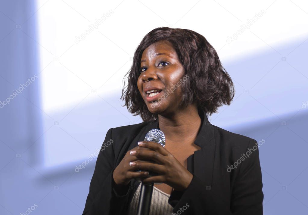  confident black African American business woman with microphone speaking in auditorium at corporate event or seminar giving motivation and success coaching
