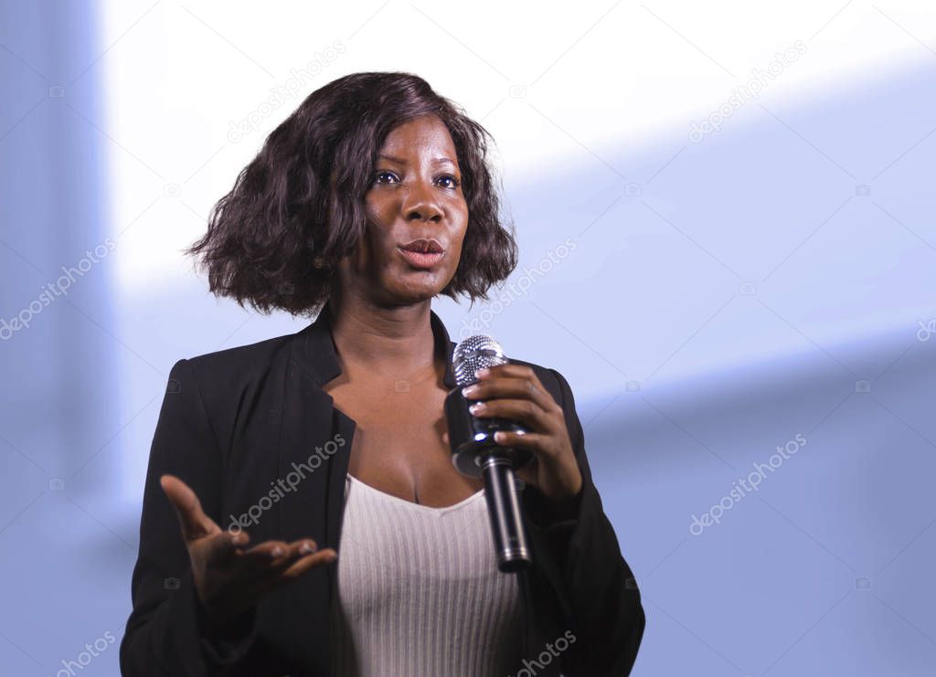  confident black African American business woman with microphone speaking in auditorium at corporate event or seminar giving motivation and success coaching