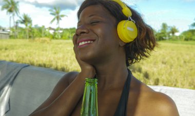 güzel ve mutlu siyah afro Amerikalı kadın müzik açık havada için dinlerken kulaklık ile soğutulmuş ve neşeli içki bira gülümseyen yaz tatili zevk rahat