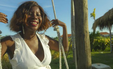 mutlu ve güzel genç Afro-Amerikan kadın siyah tropikal tatil sallanan salıncak neşeli gülümseyen üzerinde açık ve rahat olması oynarken yazlık elbise içinde eğlenceli