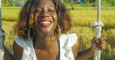 mutlu ve güzel genç Afro-Amerikan kadın siyah tropikal tatil sallanan salıncak neşeli gülümseyen üzerinde açık ve rahat olması oynarken yazlık elbise içinde eğlenceli