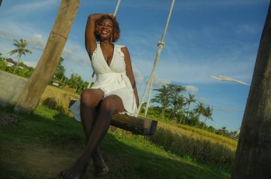 Genç mutlu ve güzel siyah afro Amerikan elbiseli kadın salıncak neşeli gülümseyen üzerinde açık ve rahat olması oynarken yaz tropikal arka planda sallanmak eğlenceli