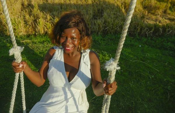 Jovem feliz e bonita negra afro-americana em vestido de verão jogando ao ar livre no balanço sorrindo alegre e relaxado se divertindo balançando em feriados tropicais — Fotografia de Stock