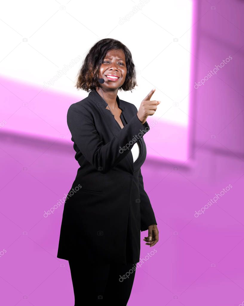confident black African American business woman with microphone speaking in auditorium at corporate seminar event giving success coaching conference or political rally