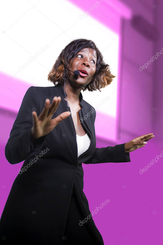 confident black afro American business woman with microphone speaking in auditorium at corporate seminar event giving success coaching conference or political rally