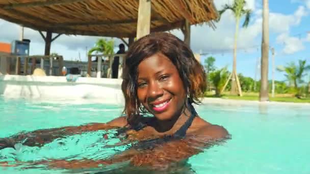 幸せで 美しい黒アフロ アメリカンの若い女性ビキニ リラックスした熱帯のビーチ リゾートのプールで楽しさと遊び心のある笑みを浮かべて明るく楽しんで夏休日豪華な旅行を持っていること — ストック動画