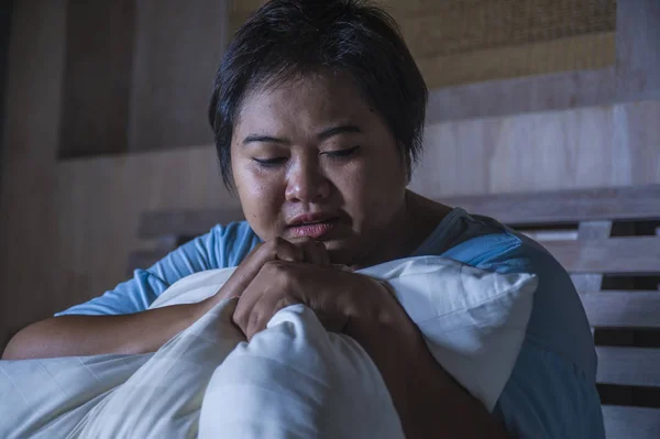 young sad and depressed fat and chubby Asian girl feeling upset and desperate crying on bed at home victim of bullying and discrimination for her plus size and overweight