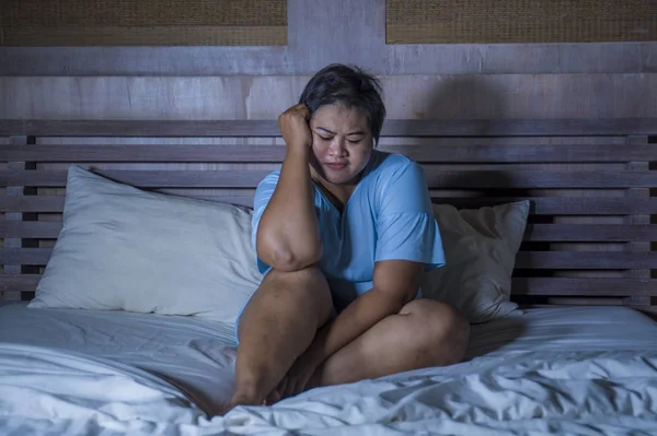 young sad and depressed fat and chubby Asian girl feeling upset and desperate crying on bed at home victim of bullying and discrimination for her plus size and overweight