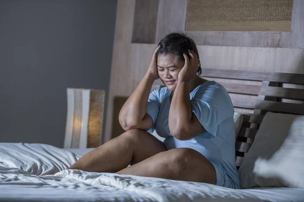 young sad and depressed fat and chubby Asian girl feeling upset and desperate crying on bed at home victim of bullying and discrimination for her plus size and overweight