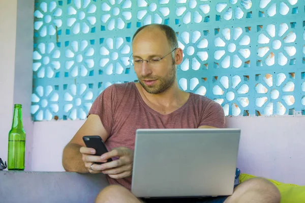 Hombre mochilero feliz y confiado que trabaja con el ordenador portátil y el teléfono móvil al aire libre relajado como empresario independiente acertado y nómada digital en trabajo del Internet — Foto de Stock