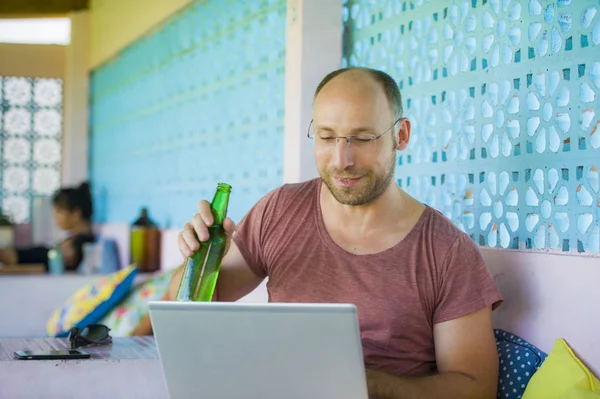 Glücklicher und selbstbewusster Backpacker, der mit Laptop im Freien arbeitet, entspannt als selbstständiger Unternehmer und erfolgreicher digitaler Nomade, der im asiatischen Café Bier trinkt — Stockfoto