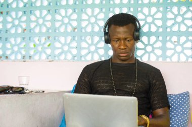 Genç serin ve hipster siyah Afro Amerikan iş adamı ağ dizüstü bilgisayar ve kulaklıklar konsantre ve düşünceli dijital göçebe internet 