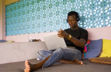 Genç serin ve hipster siyah Afro Amerikan iş adamı ağ dizüstü bilgisayar ve kulaklıklar ile konsantre ve düşünceli dijital göçebe