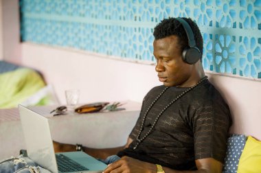 Genç serin ve hipster siyah Afro Amerikan iş adamı ağ dizüstü bilgisayar ve kulaklıklar ile konsantre ve düşünceli dijital göçebe