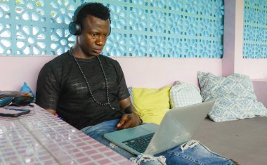 cool and hipster black afro American business man networking with laptop computer and headphones concentrated and thoughtful in digital nomad internet job