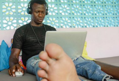 Genç serin ve hipster siyah Afro Amerikan iş adamı ağ dizüstü bilgisayar ve kulaklıklar konsantre ve düşünceli dijital göçebe internet