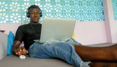 cool and hipster black afro American business man networking with laptop computer and headphones concentrated and thoughtful in digital nomad internet job