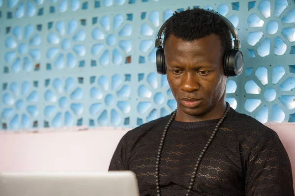 cool and hipster black afro American business man networking with laptop computer and headphones concentrated and thoughtful in digital nomad internet job