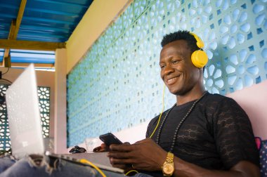 Genç mutlu ve çekici siyah Afrika Amerikan hipster adam ağ dijital göçebe iş başarı gülümseyen cep telefonu ve dizüstü bilgisayar ile rahat 