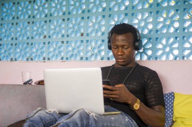 serin ve çekici siyah Afro Amerikan hipster adam kulaklık ağ cep telefonu ve dizüstü bilgisayar ile dijital göçebe iş ve internet iş rahat 