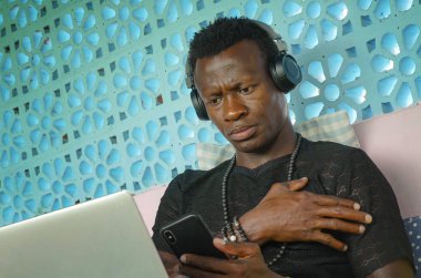 serin ve çekici siyah Afro Amerikan hipster adam kulaklık ağ cep telefonu ve dizüstü bilgisayar ile dijital göçebe iş ve internet iş rahat 