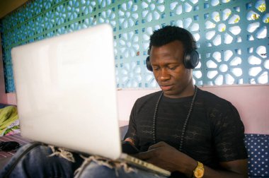 Dijital göçebe iş cep telefonu ve dizüstü bilgisayar ile rahat kulaklık ağ ile genç serin ve çekici siyah Afrikalı Amerikan hipster adam