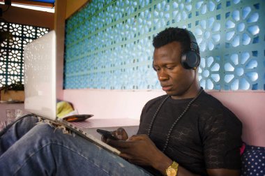 Dijital göçebe iş cep telefonu ve dizüstü bilgisayar ile rahat kulaklık ağ ile genç serin ve çekici siyah Afrikalı Amerikan hipster adam