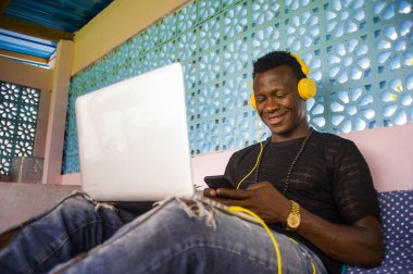 Genç mutlu ve çekici siyah Afrika Amerikan hipster adam ağ dijital göçebe iş başarı gülümseyen cep telefonu ve dizüstü bilgisayar ile rahat 
