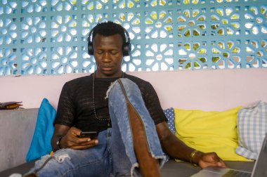 Dijital göçebe iş cep telefonu ve dizüstü bilgisayar ile rahat kulaklık ağ ile genç yakışıklı ve serin siyah Afrikalı Amerikan hipster adam