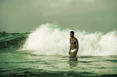 çekici ve uygun siyah Afro Amerikan adam seksi kaslı vücut ve Sixpack ABS güzellik ve sağlık konsepti etrafında büyük deniz dalgaları ve köpük ile sahilde serin poz