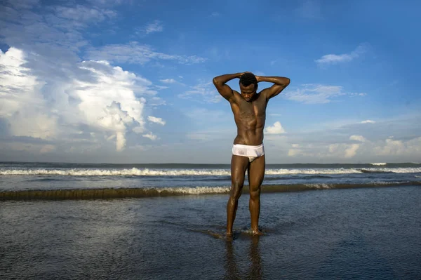 Retrato de joven atractivo y en forma negro hombre afroamericano con cuerpo musculoso fuerte posando actitud modelo fresco en la playa aislado en el cielo azul de verano — Foto de Stock