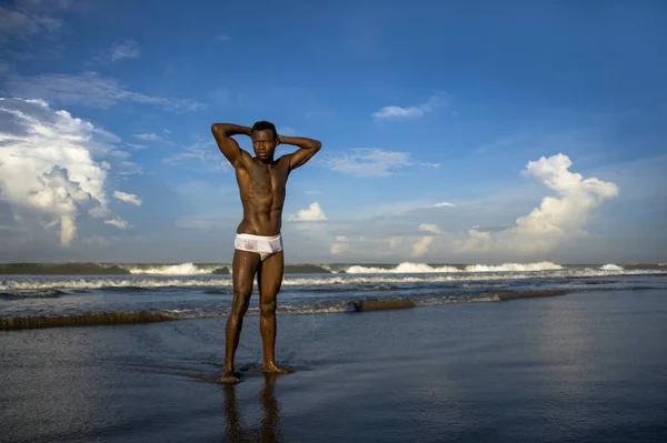 Portrait of young attractive and fit black afro American man with strong muscular body posing cool model attitude on the beach isolated on Summer blue sky — Stock Photo, Image