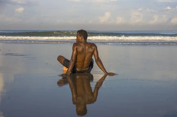 Junge attraktive und entspannte schwarzafrikanisch-amerikanische Mann mit fittem Körper und muskulösem Rücken sitzt am Strand Sand genießen schöne Aussicht denken und meditieren kostenlos — Stockfoto