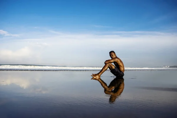 Young attractive and relaxed black afro American man with fit body and muscular back sitting on beach sand enjoying beautiful view thinking and meditating free — Stock Photo, Image