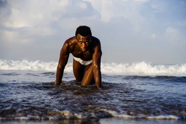 Joven atractivo y sexy negro hombre afroamericano con cuerpo muscular atlético posando fresco en el agua de mar en la playa del desierto en la belleza masculina y el concepto de plasticidad — Foto de Stock