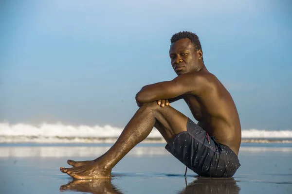 Joven atractivo y relajado negro afroamericano hombre con el cuerpo en forma y la espalda muscular sentado en la arena de la playa disfrutando de hermosa vista pensando y meditando gratis — Foto de Stock