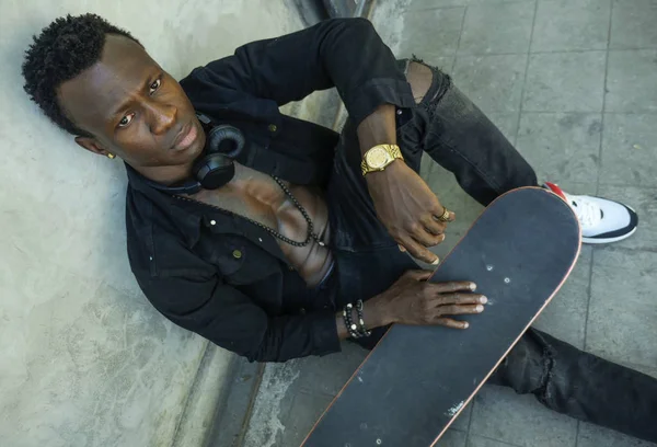 Cool isolé portrait de jeune attrayant et confiant hipster noir afro américain homme penché sur le mur de la rue tenant skate board comme badass guy dans le style urbain — Photo