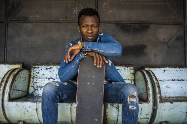 Genç yakışıklı ve çekici siyah Afrika Amerikan kaykaycı adam şehir grunge Bench tutmak paten kurulu serin tutum poz üzerinde oturuyor