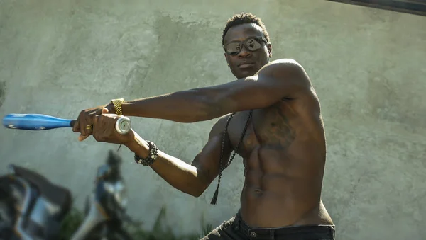 urban portrait of young aggressive and upset violent black afro American man using baseball bat threatening at grunge corner in street violence and youth gangs