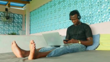 Genç serin ve çekici siyah Afro Amerikan hipster adam kulaklık ağ cep telefonu ve dizüstü bilgisayar ile dijital göçebe iş ve internet iş yaşam tarzı ile rahat