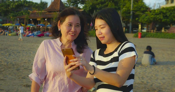 Jovem feliz e bonita menina chinesa asiática na praia tirando foto selfie com sua mãe, uma mulher madura dos anos 60, desfrutando de férias de verão viajar juntos — Fotografia de Stock