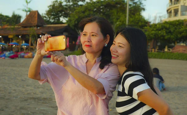 ビーチでの若い幸せとかなりアジアの中国人の女の子は、彼女の母親、60年代の成熟した女性と一緒に自分撮り写真を撮って、夏の休暇を楽しんで旅行 — ストック写真