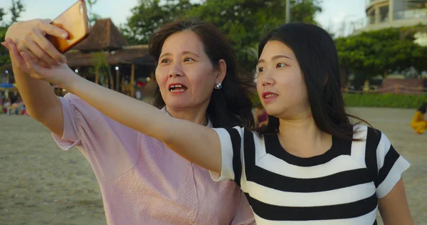 Jovem feliz e bonita menina chinesa asiática na praia tirando foto selfie com sua mãe, uma mulher madura dos anos 60, desfrutando de férias de verão viajar juntos — Fotografia de Stock