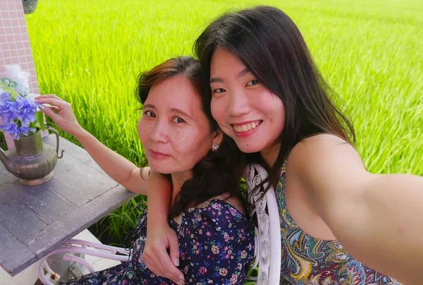 Joven feliz y bonita asiática china chica tomando foto selfie al aire libre con su madre, una mujer madura de los años 60, disfrutando de vacaciones de verano viajan juntos —  Fotos de Stock