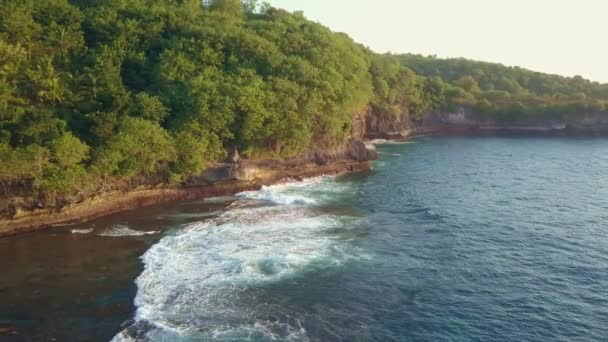 熱帯のビーチと緑の山の崖上の美しいバリ島の上にドローンと空中プルバックショット夏の休日の旅行や観光地のコンセプト — ストック動画