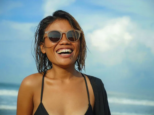 head and shoulders lifestyle portrait of young beautiful and sexy Asian girl in bikini and sunglasses enjoying holidays at tropical beach posing cool smiling happy at the sea