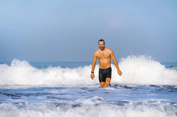 Jovem homem atraente e feliz com barba e calções de banho na praia do deserto paraíso tropical sozinho brincalhão e alegre na água do mar desfrutando de férias de verão — Fotografia de Stock