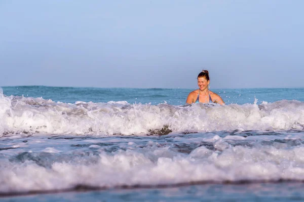 Junge fröhliche und verspielte Frau mit roten Haaren im Bikini schwimmt auf dem Meer und spielt mit großen Wellen und genießt den Sommerurlaub am paradiesischen Strand entspannt und aufgeregt im Reiseziel — Stockfoto