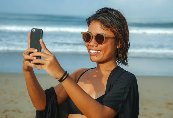 年轻、快乐、迷人的亚洲异国情调女子在海滩上自拍，手持手机，开心地笑着在美丽的热带岛屿度假 — 图库照片